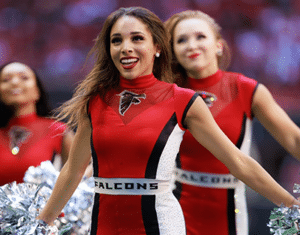 A cheerleader in a red uniform jumpsuit smiles and cheers.