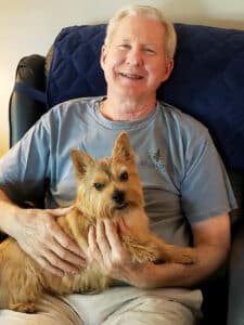 Bob Becker sitting in a chair with a cute small tan dog in his lap.